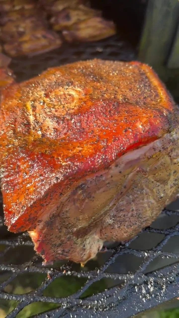 A pork shoulder on the smoker grate with a dark peppered bark
